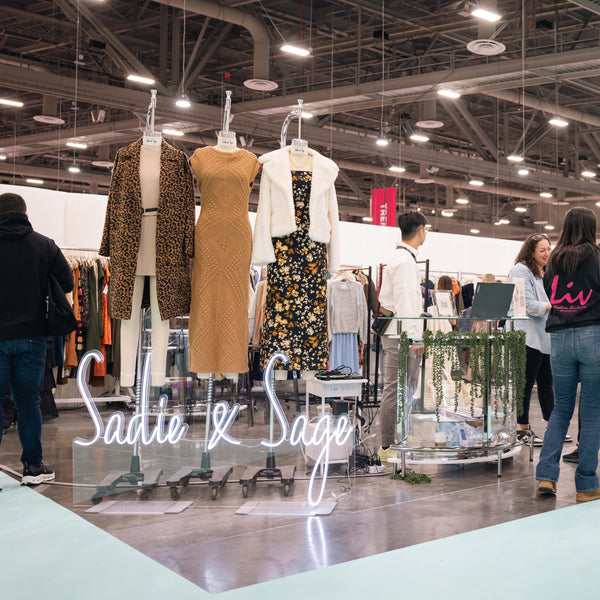 Display of clothing with 'Sadie & Sage' branding at a trade show.